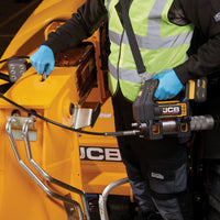 Pracownik w kamizelce odblaskowej smarujący maszynę JCB smarownicą akumulatorową 18PGG-VS z paskiem na ramię w zestawie