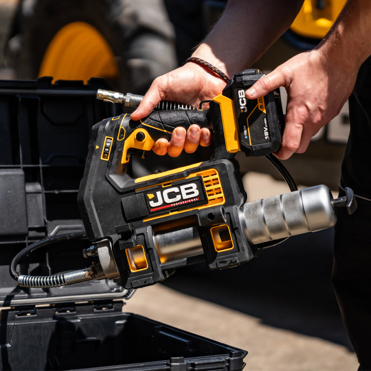 Smarownica akumulatorowa JCB 18PGG-VS trzymana w dłoni nad skrzynią narzędziową maksymalne ciśnienie 700 bar